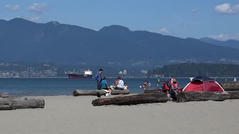 A-father-with-child-on-beach-and-kids-playing-by-tent-with-ship-in-distance