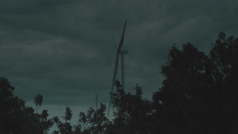 Static-view-of-large-wind-turbine-alone-in-field-above-forest-on-grey-cloudy-day