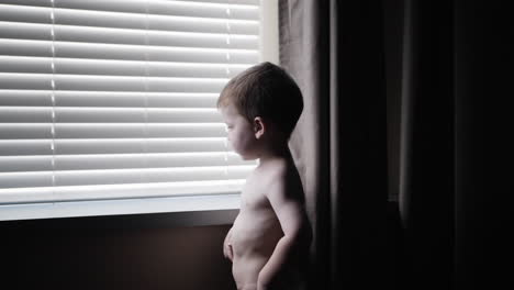 Young-boy,-child-walks-in-slow-motion-and-looks-out-window