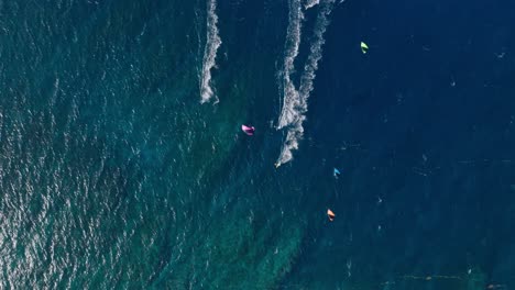 Four-Kiteboarders-Kitesurfing-Together,-Top-Down-Wide-Angle-CInematic-Aerial-Shot,-Tropical-Blue-Water,-Paradise,-Slow-Motion