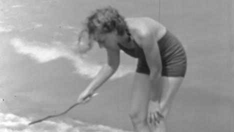 1930er-Jahre-Elegante-Frau-Im-Badeanzug-Schreiben-Im-Sand-Am-Strand