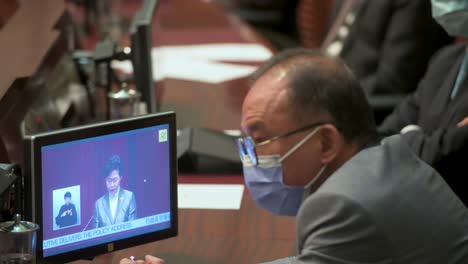 A-lawmaker-listens-to-Carrie-Lam,-former-Hong-Kong-chief-executive,-seen-on-a-screen-as-she-delivers-her-annual-policy-address-at-the-Legislative-Council-Chamber-in-Hong-Kong