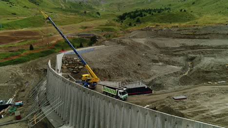 Aerial-drone-shot-of-a-crane-working-on-the-construction-of-a-dam-in-the-mountains