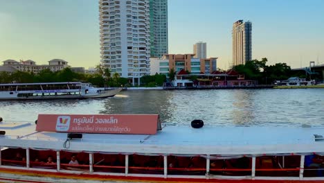 Dolly-shot-of-boats-moving-on-Chaopraya-River-in-Bangkok,-Thailand-during-sunset