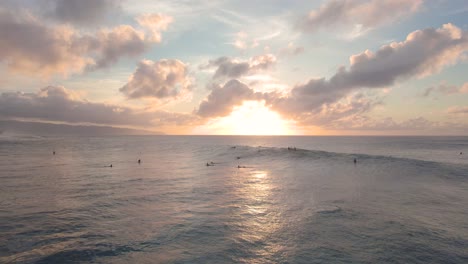 Flying-above-pacific-ocean-at-Hawaii,-surfers-float-in-water-and-catch-wave