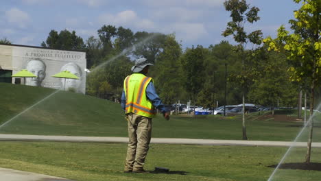 Male-worker-standing-beside-ground-sprinkler-at-park