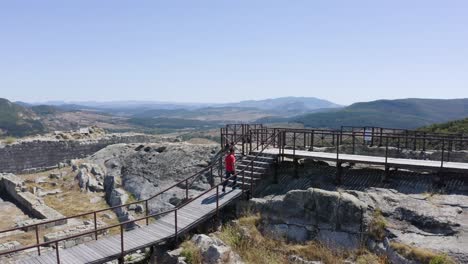 Orbiting-drone-shot-showing-a-man-walking-towards-a-water-reservoir-through-a-ramp-of-wooden-planks-on-top-of-the-ancient-city-of-Perperikon-in-the-province-of-Kardzhali-in-Bulgaria
