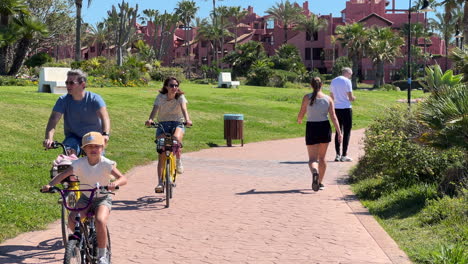 Menschen,-Die-An-Einem-Sonnigen-Tag-In-Der-Nähe-Des-Strandes-Von-Estepona-Spazieren-Gehen-Und-Fahrrad-Fahren,-Palmen-Und-Blauer-Himmel,-Lustiger-Urlaub-In-Spanien,-Paseo-Maritimo,-4K-Aufnahme