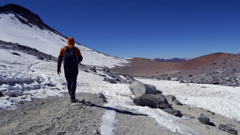 Lone-hiker-walks-toward-distant-mountain-summit-ridge-thru-snow-patch