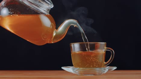 Herbal-tea-being-poured-from-a-cup-into-a-glass,-contrasted-against-a-dark-backdrop,-illustrating-the-cultural-ritual-and-hospitality-of-tea-serving