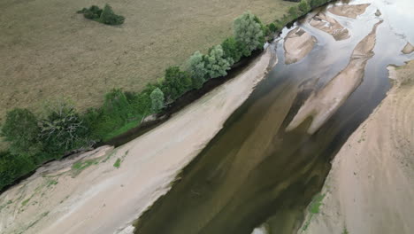 Die-Aufwärtsneigung-Zeigt-Die-Luftaufnahme-Des-Flusses,-Der-Durch-Ein-Feld-Neben-Sandbänken-Fließt