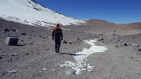 Hiker-walks-on-barren-snowy-alpine-mountain-plateau-in-Chile-Andes