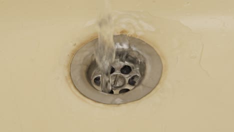 Water-flowing-down-the-sink-drain,-wasting-water