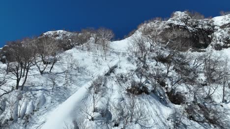 Ascending-shot-flying-up-snow-covered-mountain-cliff-face,-establishing-shot-revealing-massive-mountains