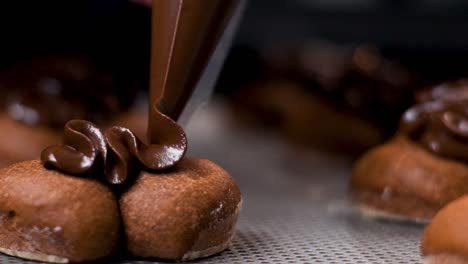 Close-up-slow-motion-clip-of-melted-chocolate-being-piped-onto-round-biscuits-on-metal-baking-tray