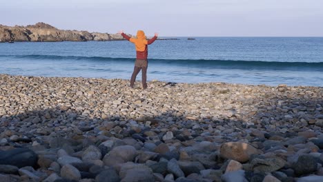 Man-enjoys-crisp,-cool-sunny-morning-on-rocky-ocean-beach,-stretching