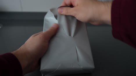 Closeup-of-mystery-box-with-question-mark-on-a-grey-package-paper,-hands-opening