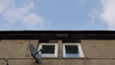 Blue-sky-above-two-windows,-building-and-TV-aerial,-low-angle-on-sunny-day