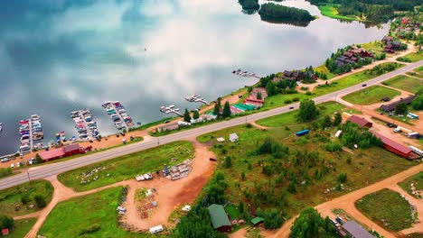 Aerial-Drone-Rising-Motion-of-Beautiful-Clear-Blue-Lake-Water-with-Sky-Reflection-next-to-Houses-and-Cars-Driving-on-Road-by-Boat-Docks-in-Grand-Lake-Colorado-during-Summer-in-the-Rocky-Mountains