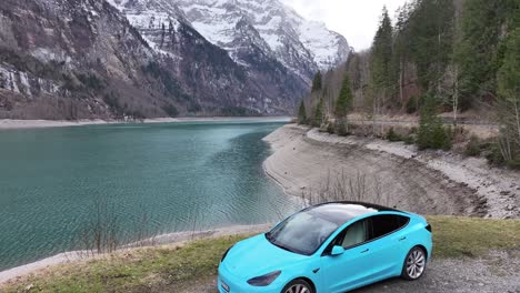 Tesla-Modelo-3-Azul-Eléctrico-En-La-Carretera-Alpina-Junto-Al-Lago,-Klöntalersee,-Suiza