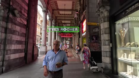 Handheld-clip-walking-along-busy-covered-walkway-with-flashing-neon-signs-and-many-tourists-and-pedestrians-passing