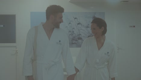 from-the-front,-a-young,-handsome,-smiling-Caucasian-couple-in-bathrobes-stroll-through-the-spa-corridors,-gazing-at-each-other-in-love,-joy-and-wonder