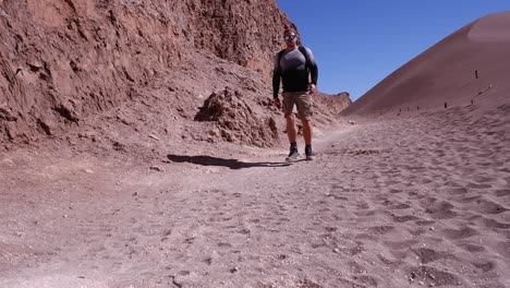 Male-hiker-walking-along-desert-sand-cliff-in-Chile-approaches-camera