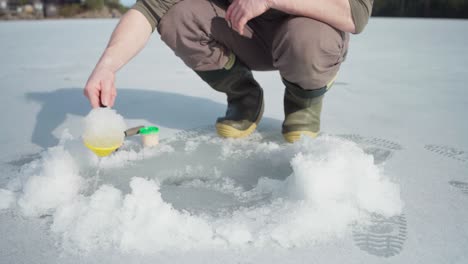 Fisherman-Removing-Ice-On-Fishing-Hole-With-Plastic-Scooper