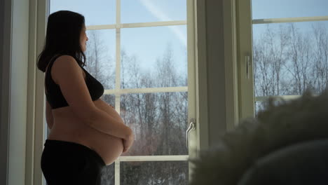 Heavily-pregnant-brunette-woman-feels-bump-by-window