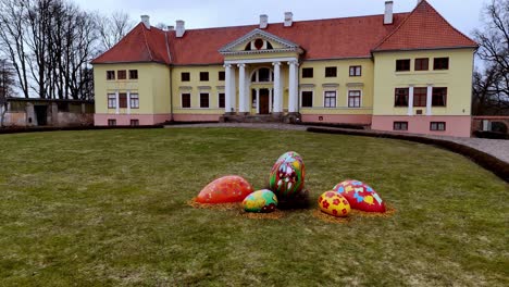 Landhaus-Mit-Orientalisch-Bemalten-Bunten-Eiern-Im-Grünen-Gartengras,-Hausbau-Im-Europäischen-Stil-In-Nordosteuropa-Mit-Roten-Fliesen,-Blassgelb-Und-Rosa-Bemalt