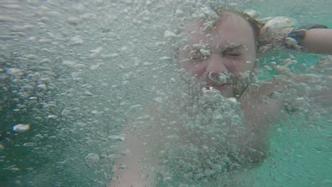 Man-submerged-underwater,-surrounded-by-bubbles,-then-surfacing-In-The-Kali-Biru-Within-Tropical-Forest-in-Raja-Ampat,-West-Papua,-Indonesia