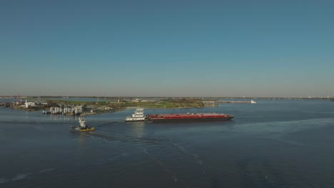 An-aerial-view-of-a-tugboat-and-barge-crossing-paths-with-the-Lynchburg-Ferry-before-sunset-on-the-Houston-Ship-Channel-in-Houston,-Texas