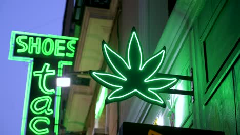 Ein-Grünes-Neon-Ladenschild-Mit-Cannabisblatt-Logo,-Das-Nachts-Eingeschaltet-Ist