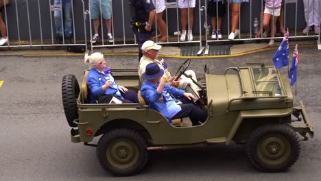 Die-Ehemaligen-Soldatinnen-Fahren-Auf-Einem-Militärfahrzeug,-Nehmen-An-Der-Traditionellen-Anzac-Day-Parade-Teil-Und-Schwenken-Der-Jubelnden-Menge-Die-Australische-Nationalflagge