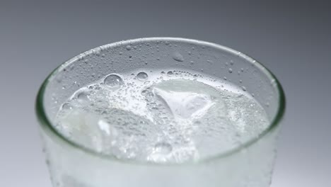 Close-up-fixed-shot-of-top-of-full-glass-of-fizzy-soda-in-a-glass-with-ice,-with-a-plain-grey-white-background