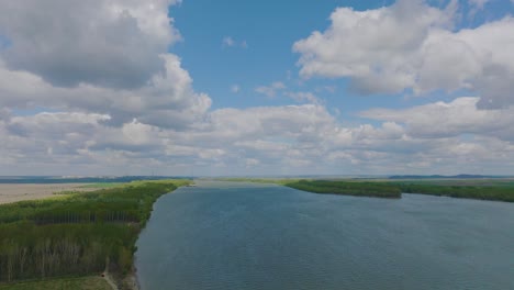 Aerial-over-a-big-european-river-showing-cloudy-blue-skies-and-green-forests-on-each-bank-of-the-river