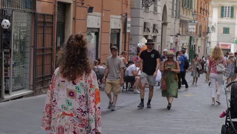 Woman-with-curly-hair-and-patterned-clothing-walking-along-busy-city-street-lines-with-houses-and-shops-in-Italy
