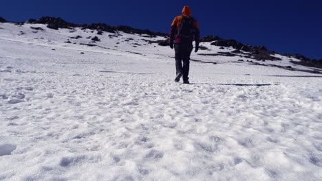 Low-angle:-Lone-hiker-walks-on-snow-toward-distant-mtn-summit-ridge