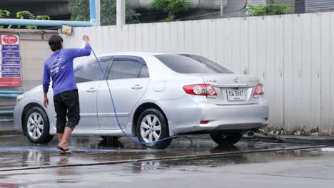 Ein-Autowascharbeiter-Sprüht-Etwas-Wasser,-Um-Den-Seifenschaum-Vom-Auto-Zu-Waschen,-Und-Reinigt-Es-In-Einer-Autowaschanlage-In-Bangkok,-Thailand