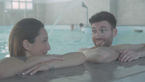 Slow-motion-shot-of-a-couple-relaxing-at-the-side-of-a-pool-and-speaking