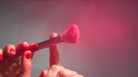 A-close-up-of-a-makeup-brush-picking-up-red-powder-from-a-stack-and-then-being-shaken-with-fingers,-releasing-powder-dust,-embodies-the-concept-of-makeup-and-beauty-in-lifestyle