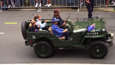 The-former-servicewoman-and-her-grandchildren-riding-on-a-military-vehicle,-participating-in-Anzac-Day-parade-tradition-and-waving-at-the-cheering-crowds