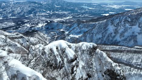 Nahaufnahme-Eines-Absteigenden-Schusses-über-Dem-Gipfel-Des-Japanischen-Myoko-Bergs,-Kamera-Fliegt-über-Dem-Rand-Einer-Schneebedeckten-Klippe