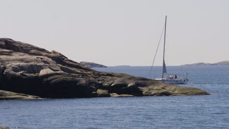 Sailboat-Vanishing-Behind-Coastal-Rocky-Shore,-Serenity-at-Sea-concept,-Wide-shot