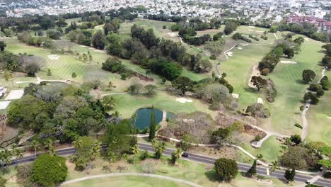Luftaufnahme-Eines-Golfplatzes-Mit-Professionellen-Spielern,-Die-Den-Sport-Ausüben,-Im-Hintergrund-Die-Stadt