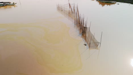 Arrow-head-fish-nets-in-muddy-brown-green-waters-on-the-Tonle-Sap-lake-shore-line,-Drone-fly-over,-Cambodia