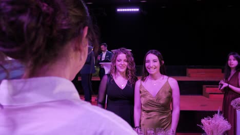 A-waitress-during-a-gala-evening-offers-glasses-of-champagne-to-two-young-student-girls,-one-dressed-in-a-black-dress-and-the-other-green