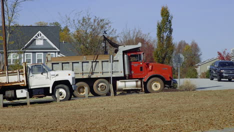 Dump-truck-reversing-slowly-down-a-hill,-then-coming-to-a-stop-near-another-dump-truck-during-a-bright-Fall-day