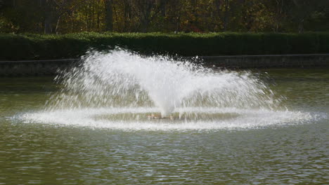 Typischer-Springbrunnen-Mit-Kegelförmigem-Sprühnebel-In-Einem-Kleinen-Teich-In-Einem-öffentlichen-Park-Im-Sommer