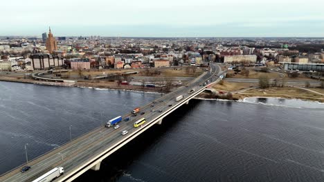 Un-Puente-Largo-Y-Curvo-Con-Múltiples-Carriles-Para-El-Tráfico-Que-Circula-En-Ambas-Direcciones-Sobre-Daygava-Tiene-Una-Parte-Inferior-Blanca-Y-Vigas-Marrones-Que-Sostienen-La-Carretera,-Con-Altas-Torres-Que-Se-Elevan-Desde-El-Agua-Debajo.